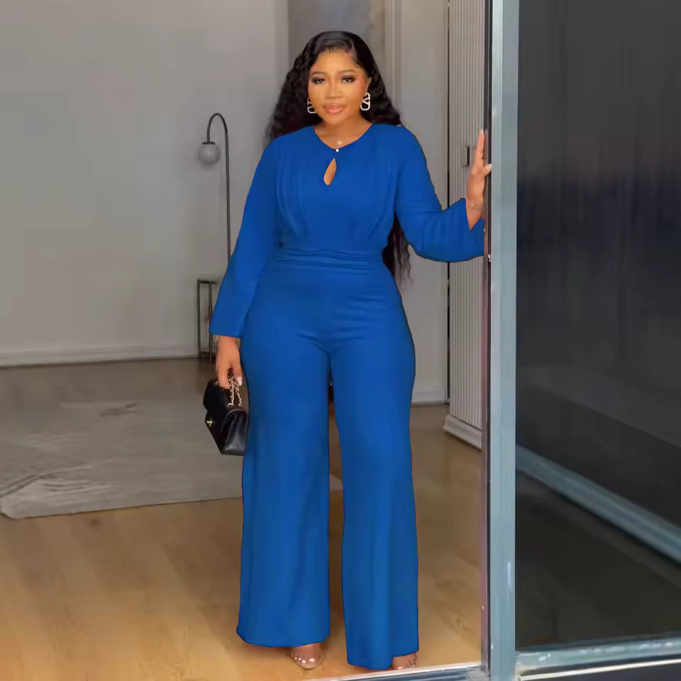 Woman in a blue jumpsuit standing in a room with a neutral background