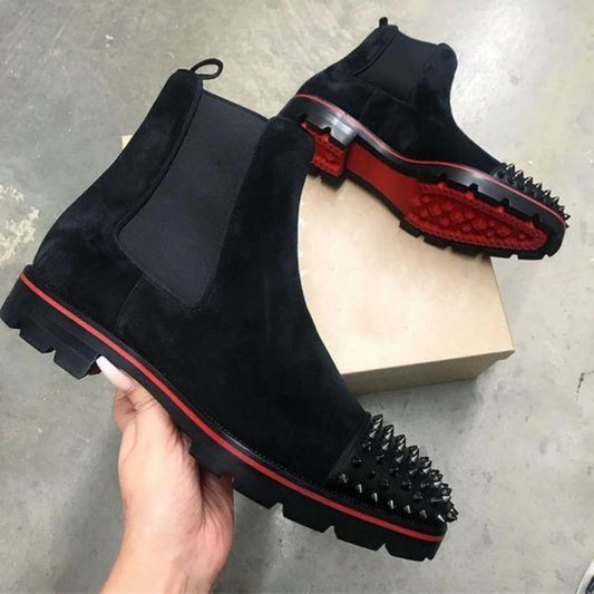 Black ankle boots with red accents held by a hand on a concrete floor.