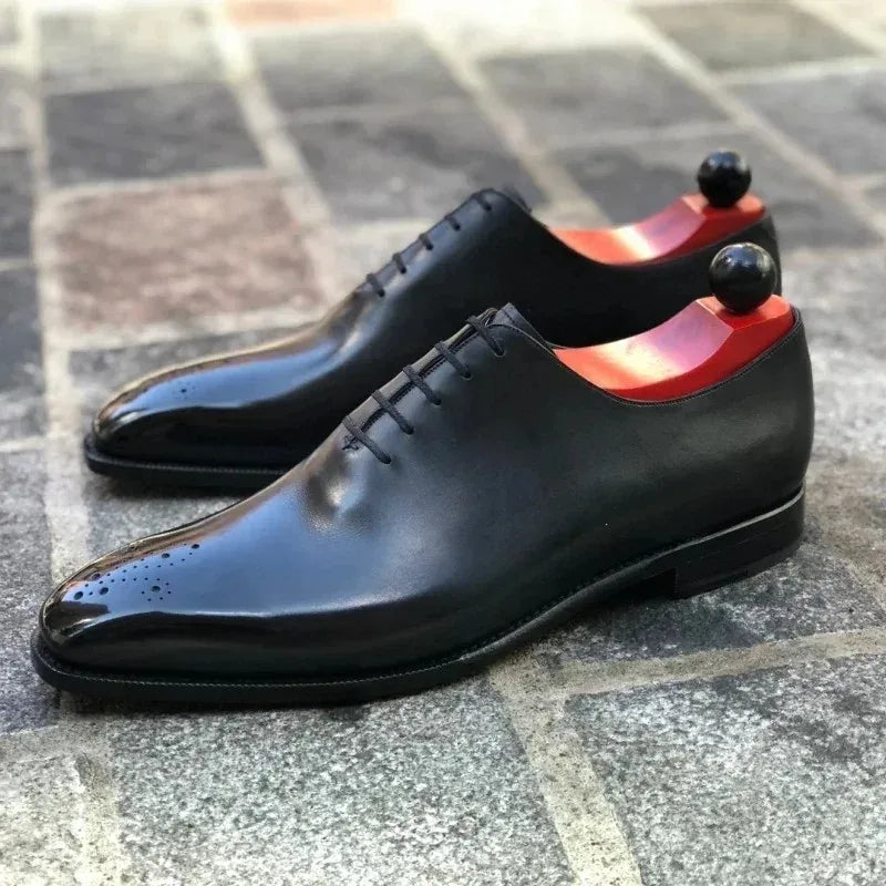Black dress shoes with red soles on a tiled floor