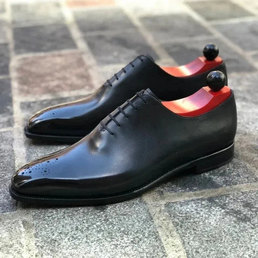 Black dress shoes with red soles on a tiled floor