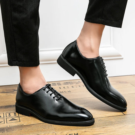 Black dress shoes worn with black pants on a wooden floor.