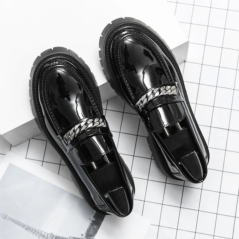 Black glossy loafers with chain detail on a white grid background