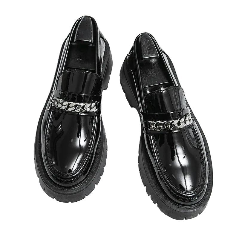 Black glossy loafers with chain detail on a grid background