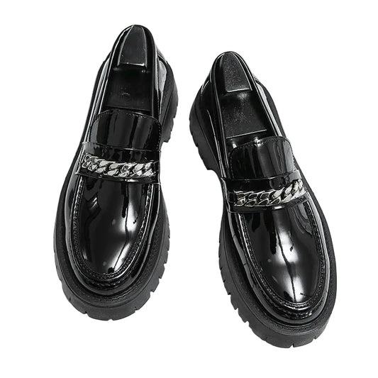 Black glossy loafers with chain detail on a grid background