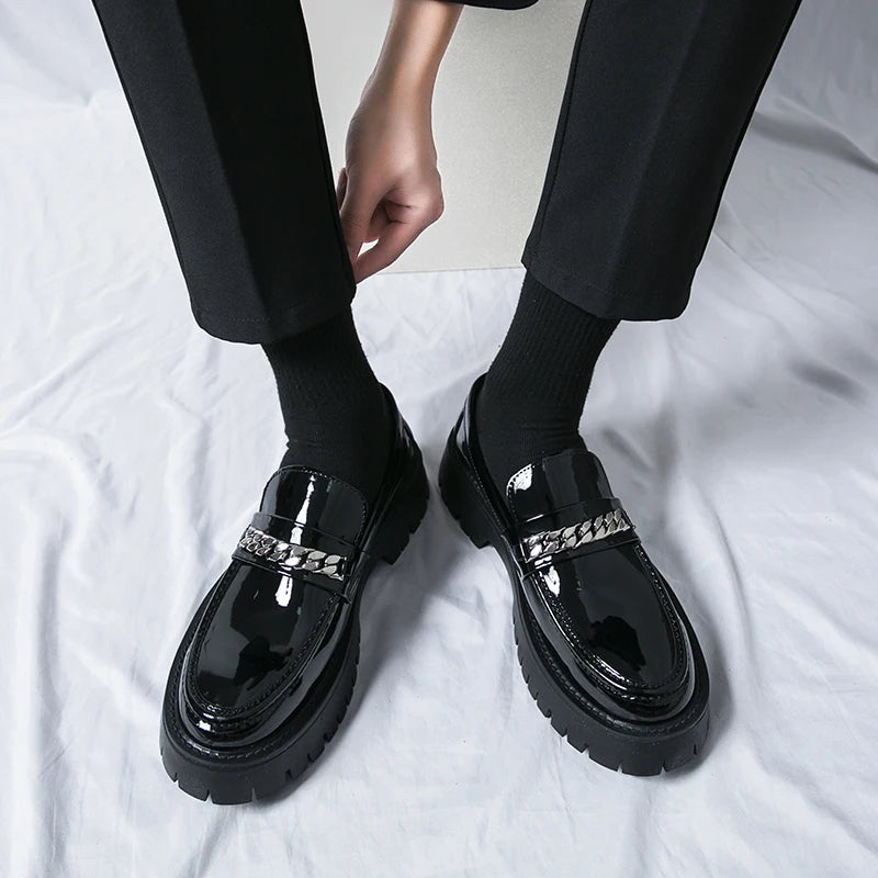 Black glossy loafers with silver accents worn by a person on a white background