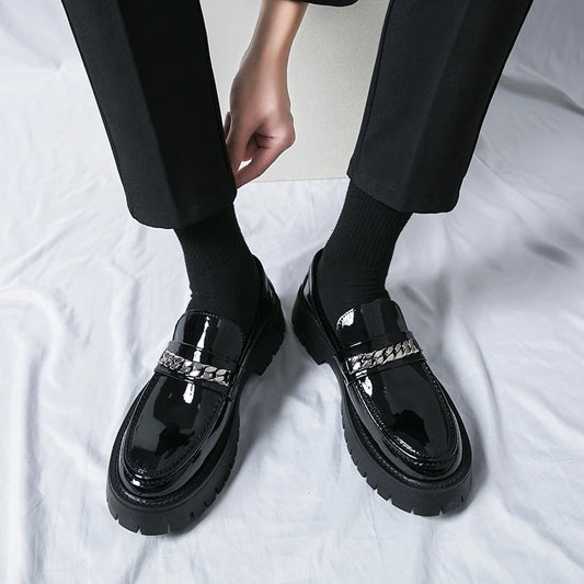 Black glossy loafers with silver accents worn by a person on a white background