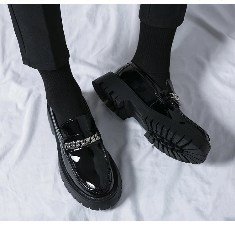 Black glossy shoes with chain details on a white fabric background