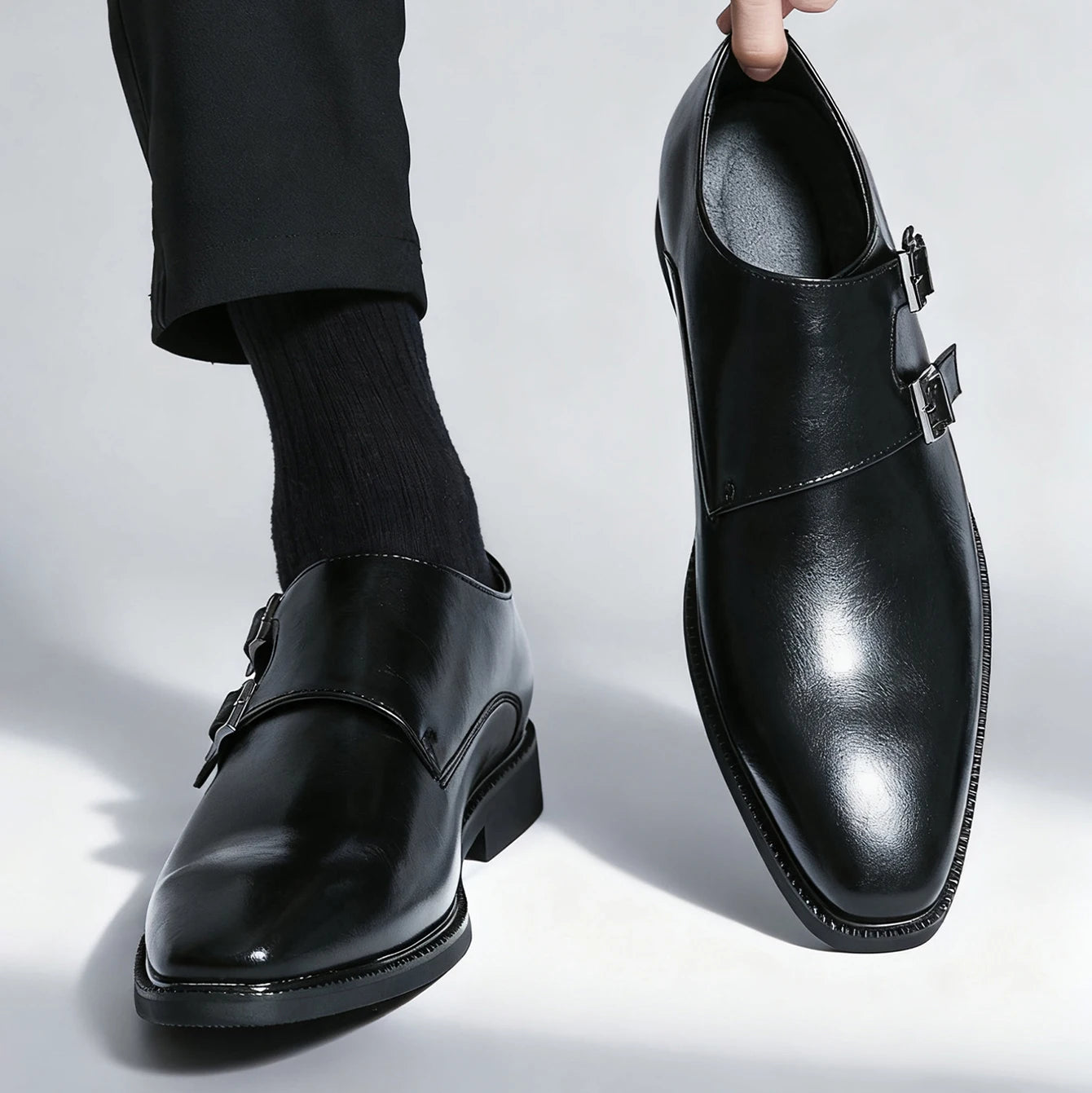 Black leather shoes with buckles worn by a person on a light gray background