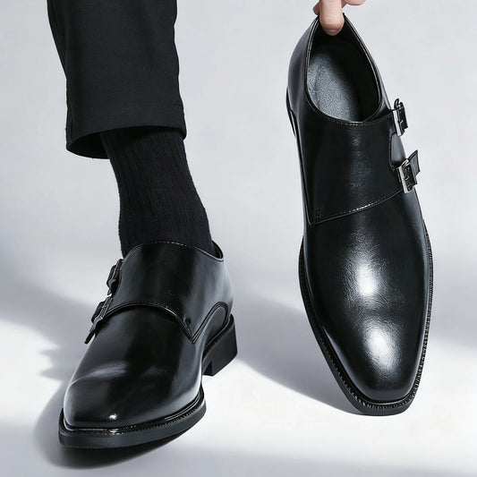 Black leather shoes with buckles worn by a person on a light gray background