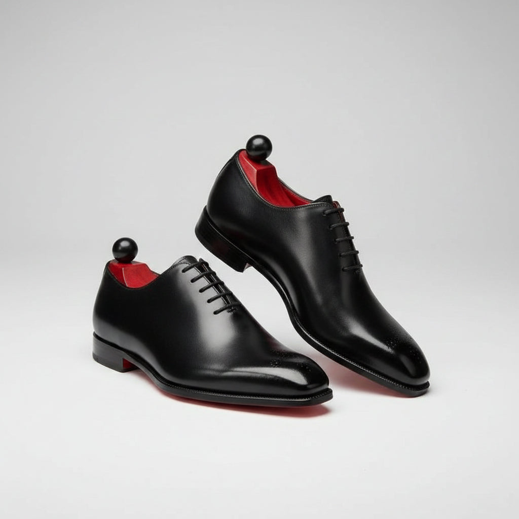 Black shoes with red soles on a concrete surface