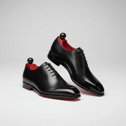 Black shoes with red soles on a concrete surface