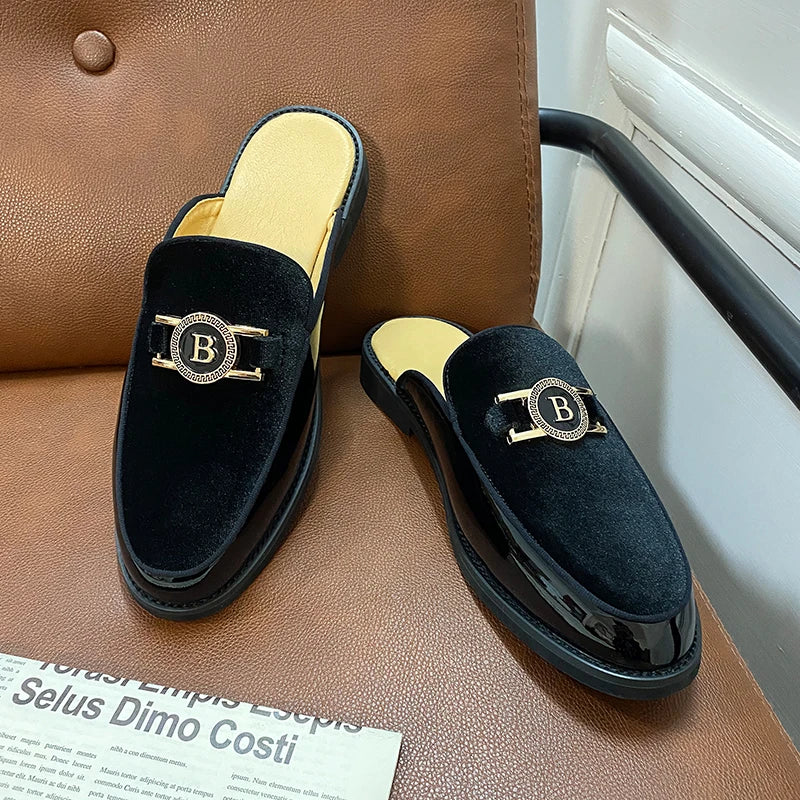 Black velvet loafers with gold 'B' emblem on a brown leather surface.