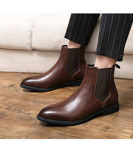 Brown leather Chelsea boots worn with black pants on a wooden floor.