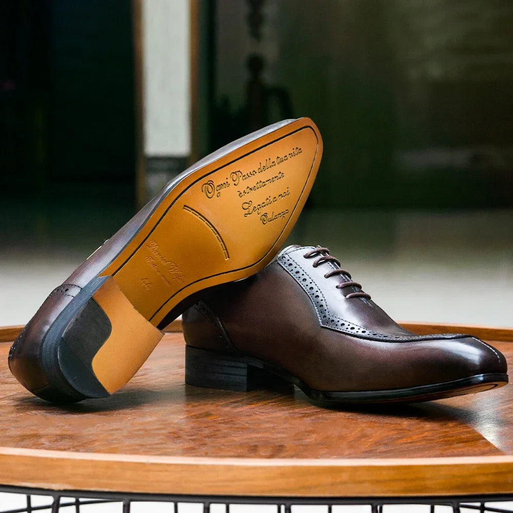 Brown leather dress shoes with yellow soles on a wooden surface