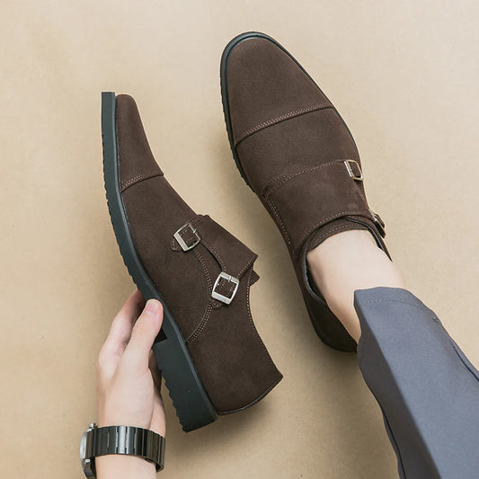 Brown monk strap shoes being held on a beige background