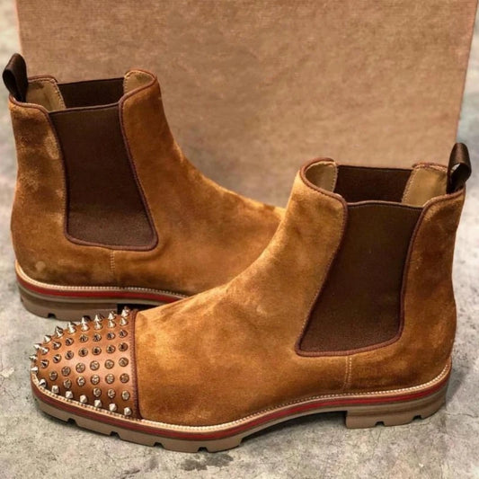 Brown suede Chelsea boots with spiked toe cap on a textured surface