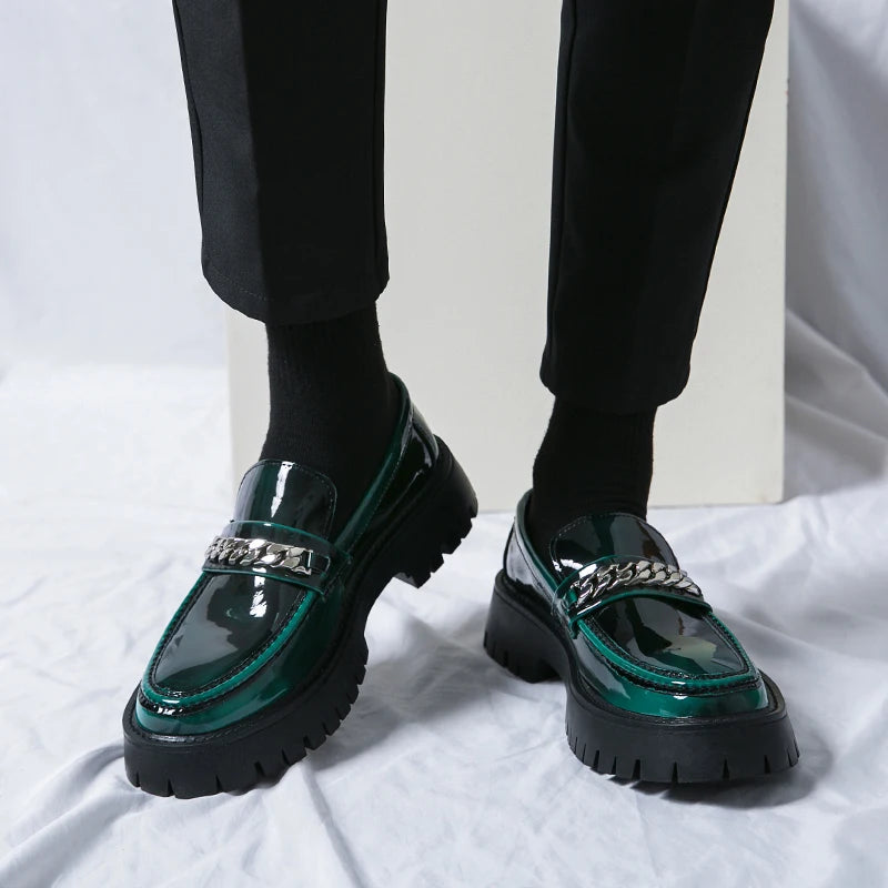 Green loafers with chain details worn with black pants on a white fabric background