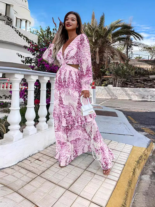 Woman in a pink floral dress standing on a tiled path with plants and a white building in the background.
