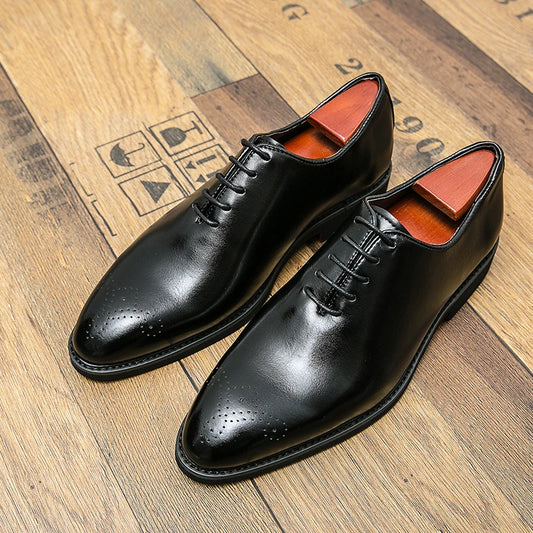 Pair of black dress shoes with orange lining on a wooden floor.