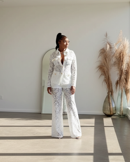 Person in a white outfit standing in a bright room with large windows and minimal decor.