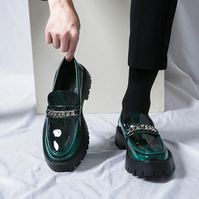 Person wearing green loafers with chain details on a white background