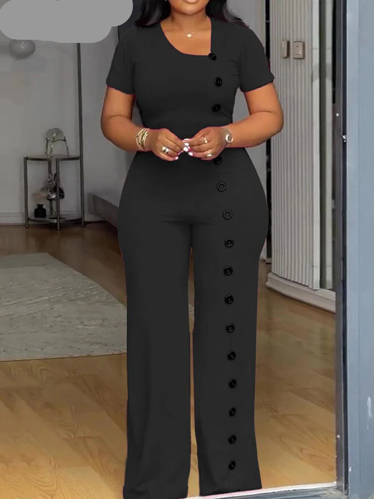 Woman wearing a black button-up outfit standing in a room with wooden floor and white walls.