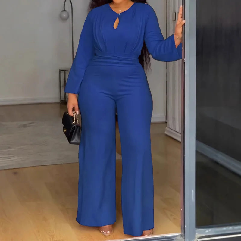 Woman in a blue jumpsuit standing in a room with a mirror.
