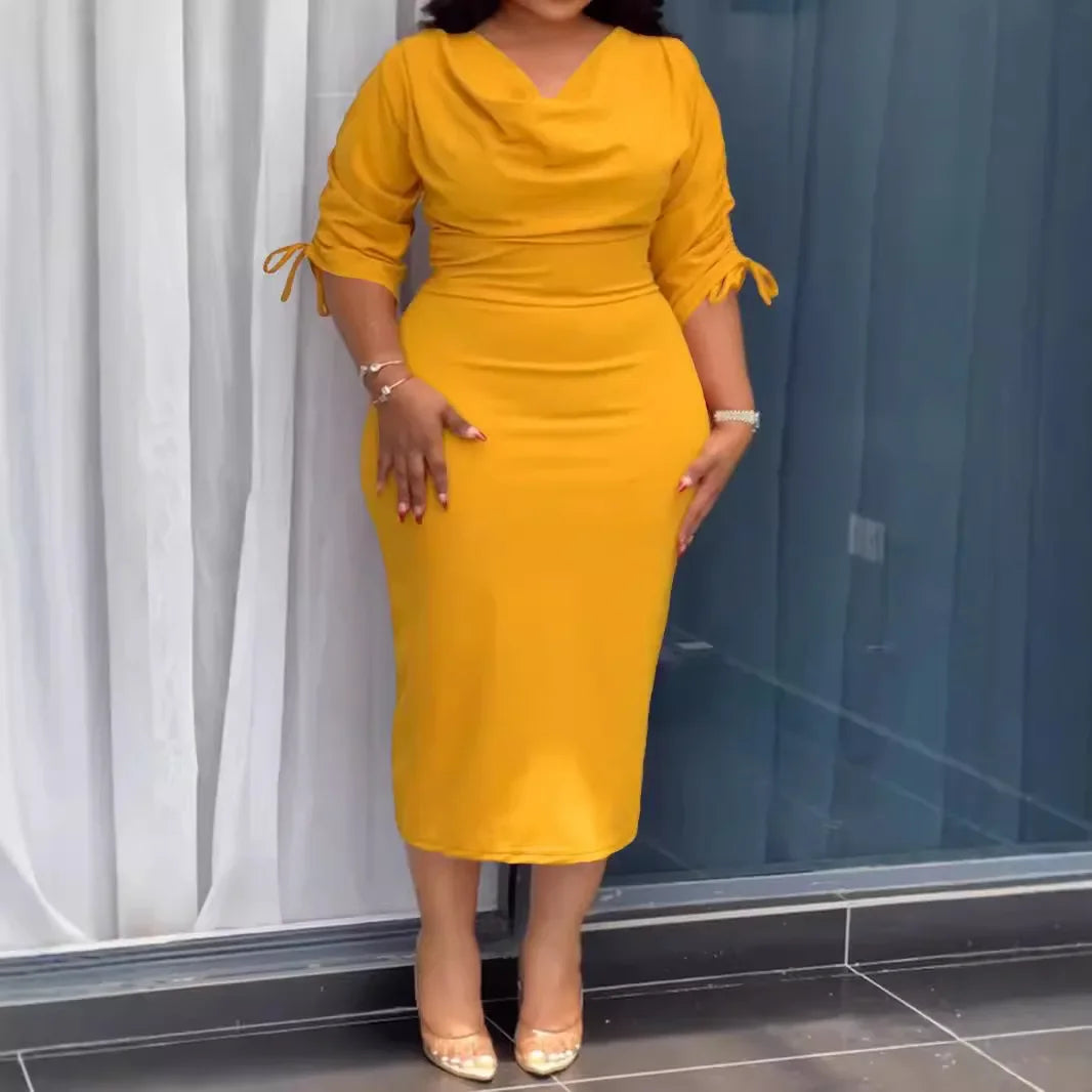 Woman wearing a yellow dress standing indoors with curtains in the background