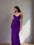 Woman in a purple dress standing in a room with a painting and light fixture on the wall.