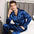 Man wearing blue satin pajamas sitting on a bed.