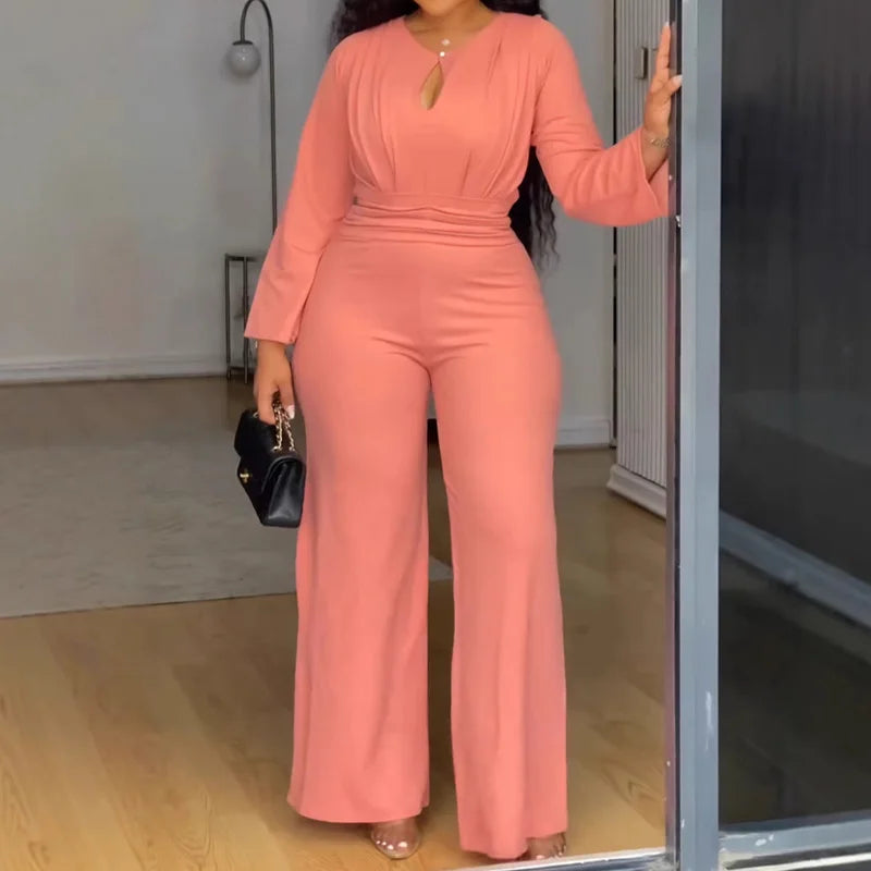 Woman in a pink jumpsuit standing in a room with a mirror.