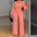 Woman in a pink jumpsuit standing in a room with a mirror.
