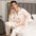 Man wearing a light pink satin pajama set sitting on a bed.