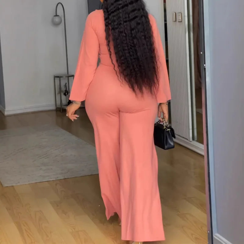 Person wearing a pink jumpsuit standing in a room with wooden flooring.