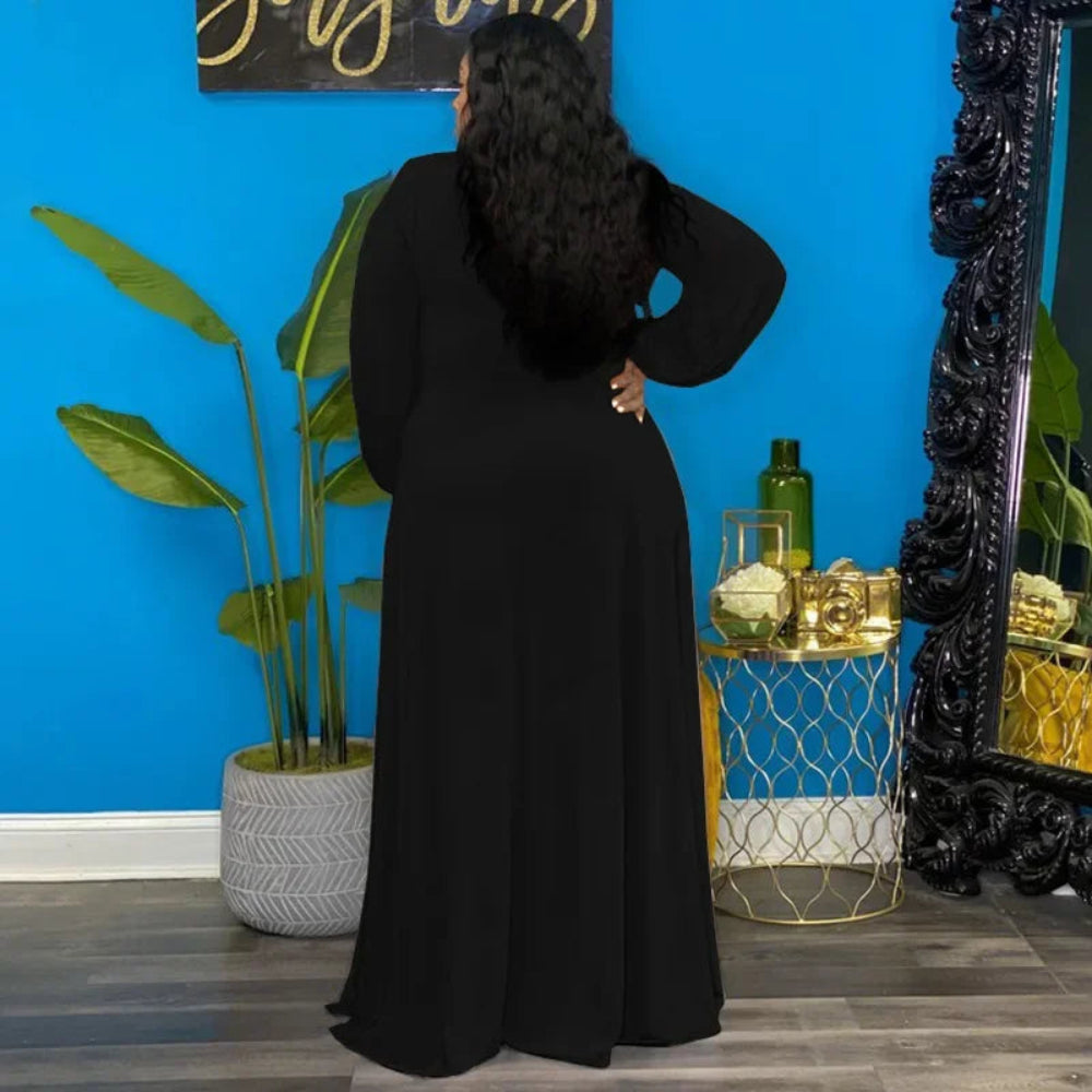 A woman dressed in black stands in front of a blue wall adorned with decorative elements.