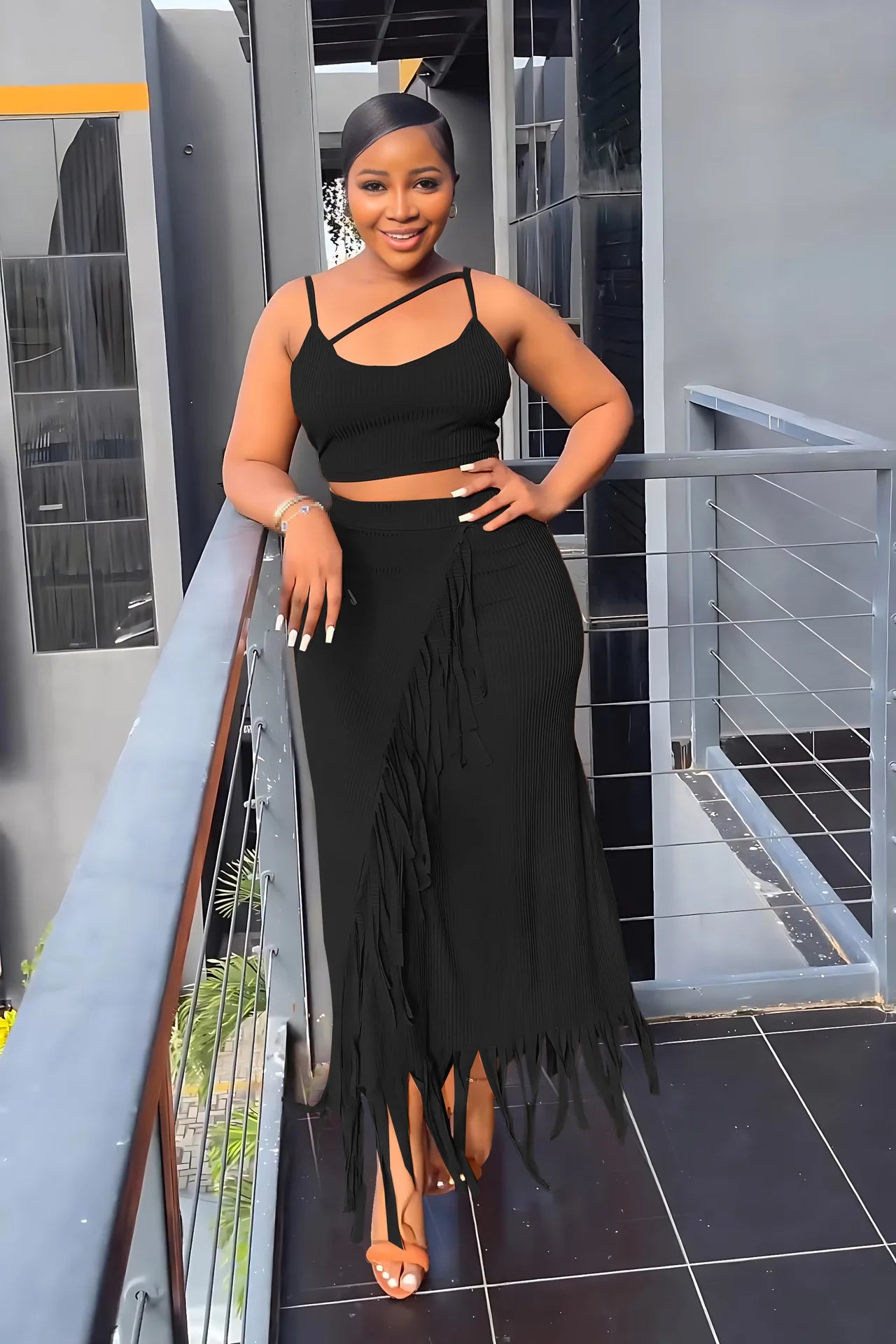 Woman in a black fringe dress standing on a balcony.