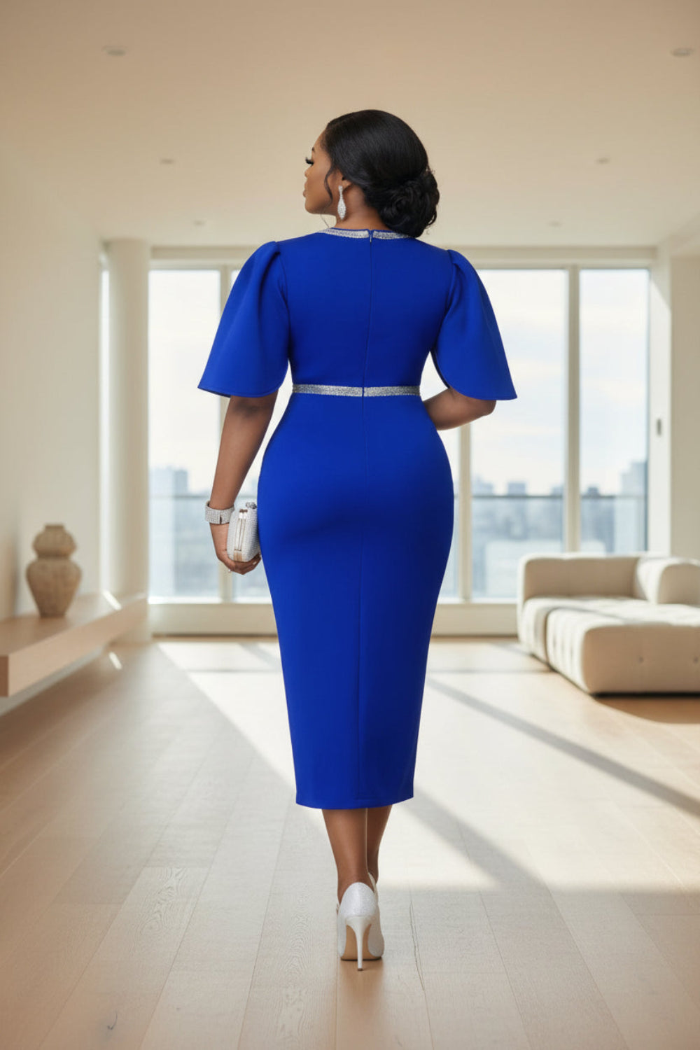 Woman in a blue dress with a silver belt standing in a formal setting with other people in elegant attire.