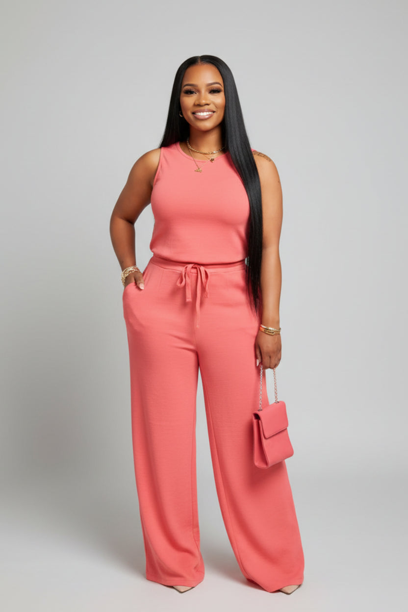 A woman in a coral jumpsuit is standing in front of a mirror with draped curtains.