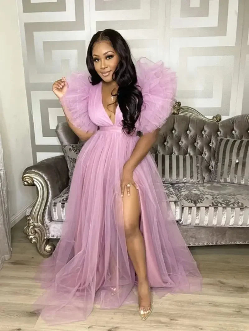 Woman in a pink dress with ruffled sleeves posing in a room with a decorative sofa.