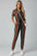 A woman wearing a striped jumpsuit is standing against a beige wall.