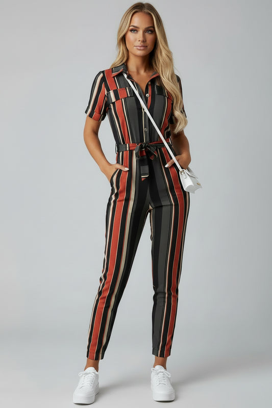 A woman wearing a striped jumpsuit is standing against a beige wall.