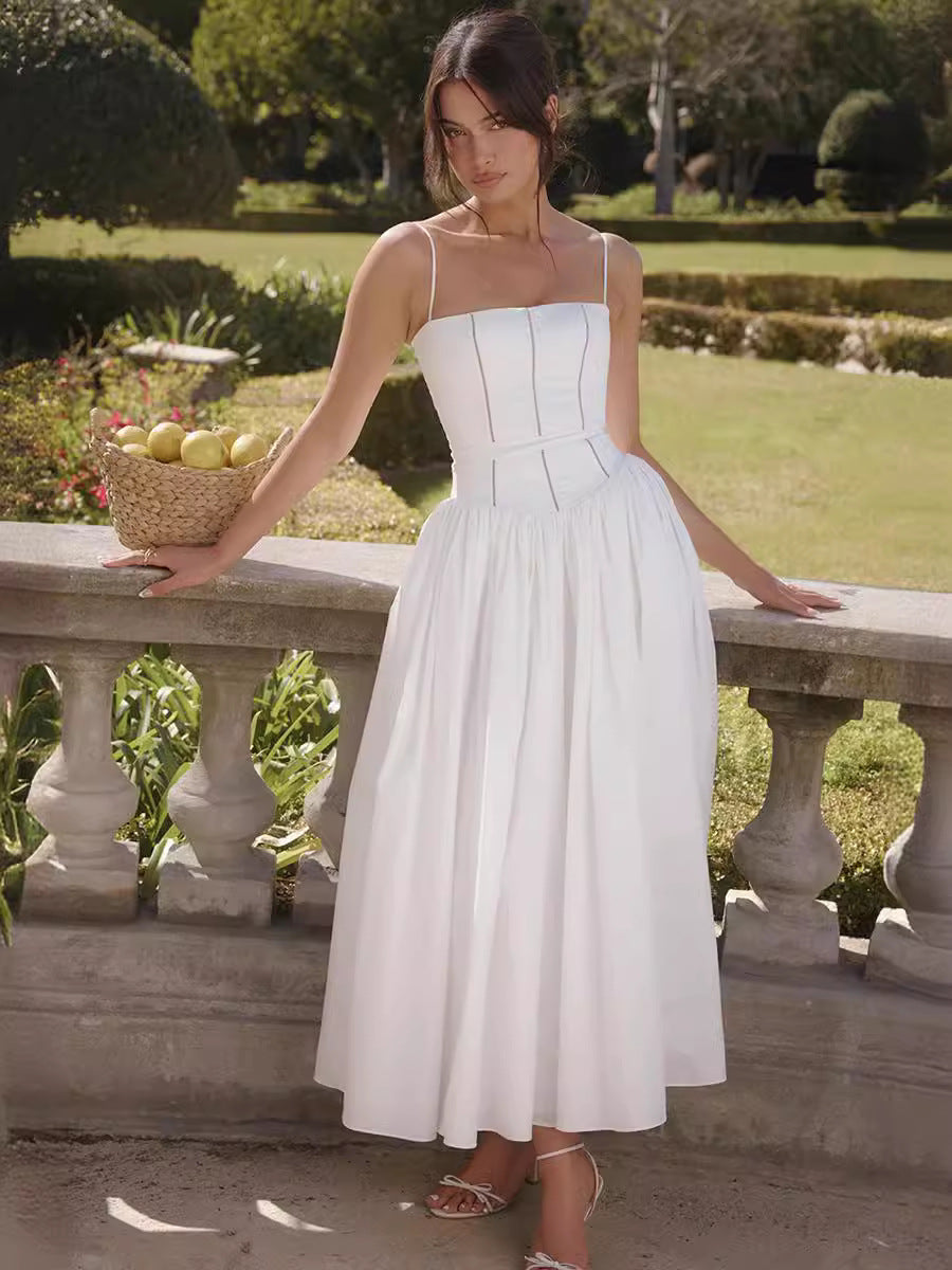 Woman in a white dress standing in a garden with a stone wall and greenery.