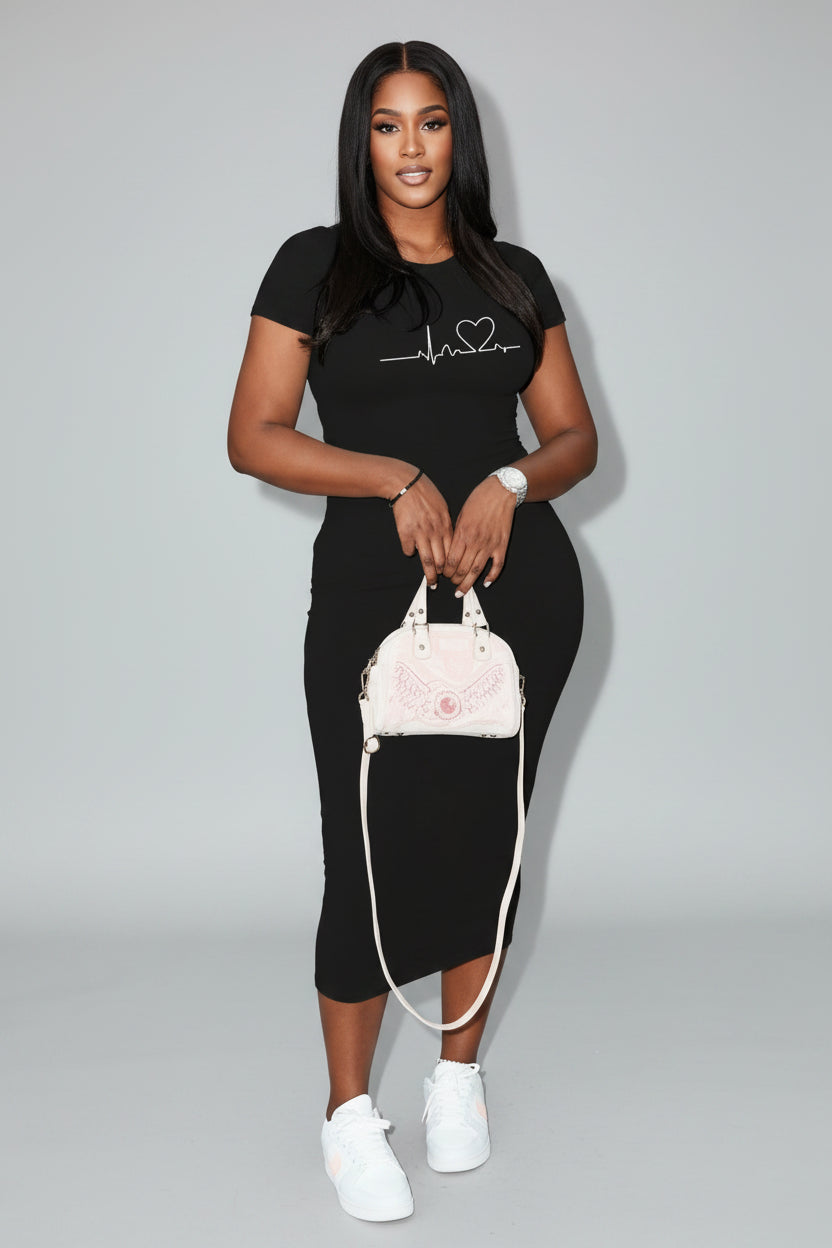 A woman in a black outfit with a heart design is holding a white handbag on a city street.