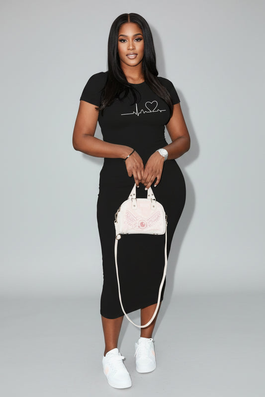 A woman in a black outfit with a heart design is holding a white handbag on a city street.