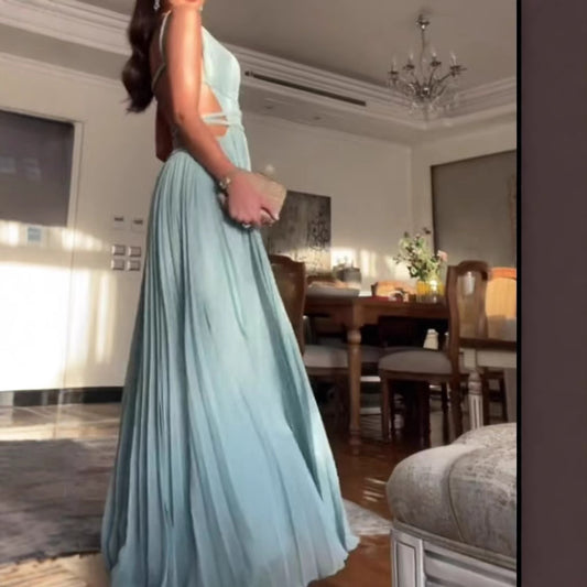 Woman in a light blue evening gown standing in a room with a dining table and chandelier.