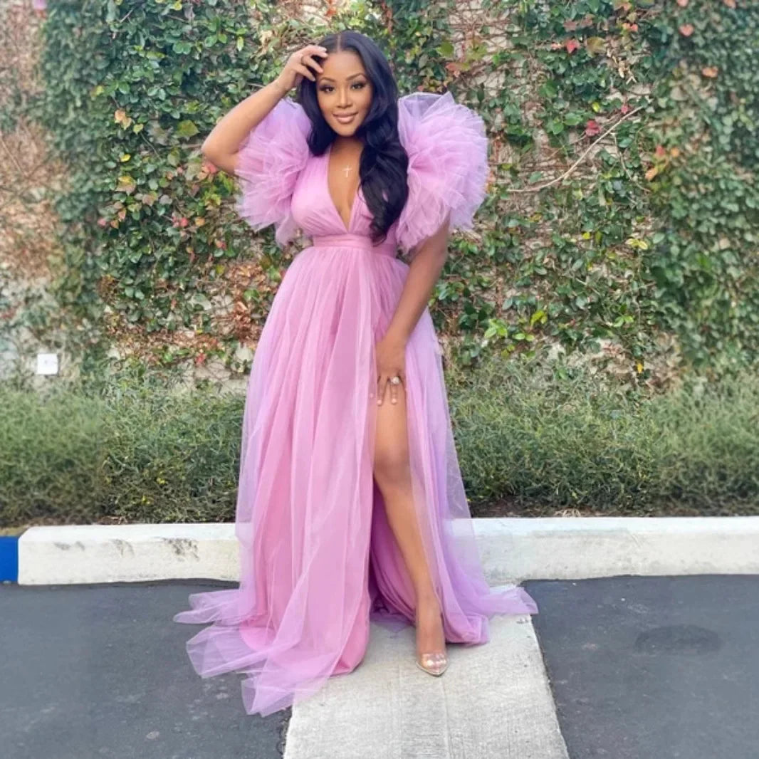 Woman in a pink evening gown standing outdoors with greenery in the background