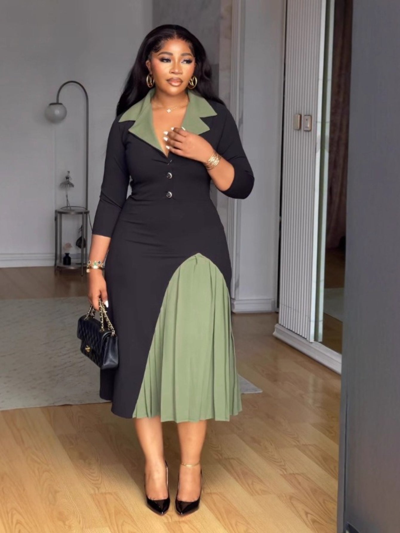 Woman wearing a black and green dress in a room with wooden flooring.