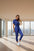 Woman in blue jumpsuit against beige wall.