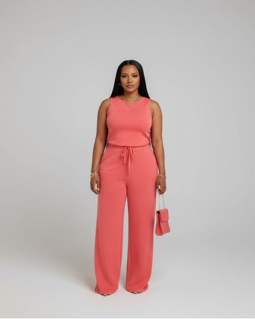 A woman wearing a coral jumpsuit is standing in front of a mirror with gold and white curtains.