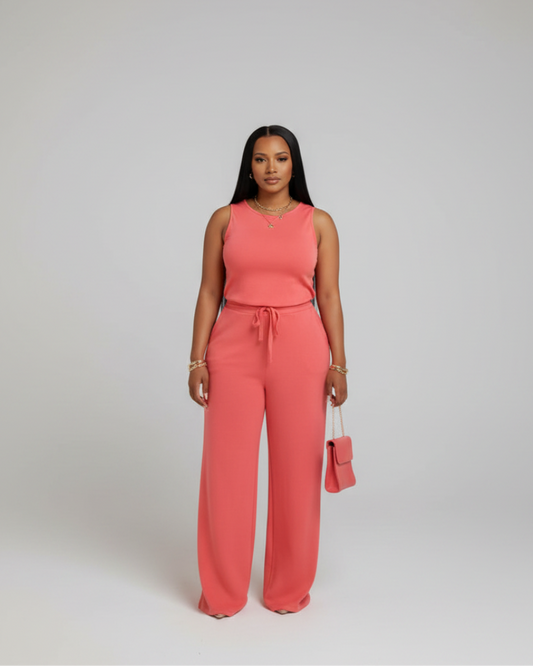 A woman wearing a coral jumpsuit is standing in front of a mirror with gold and white curtains.
